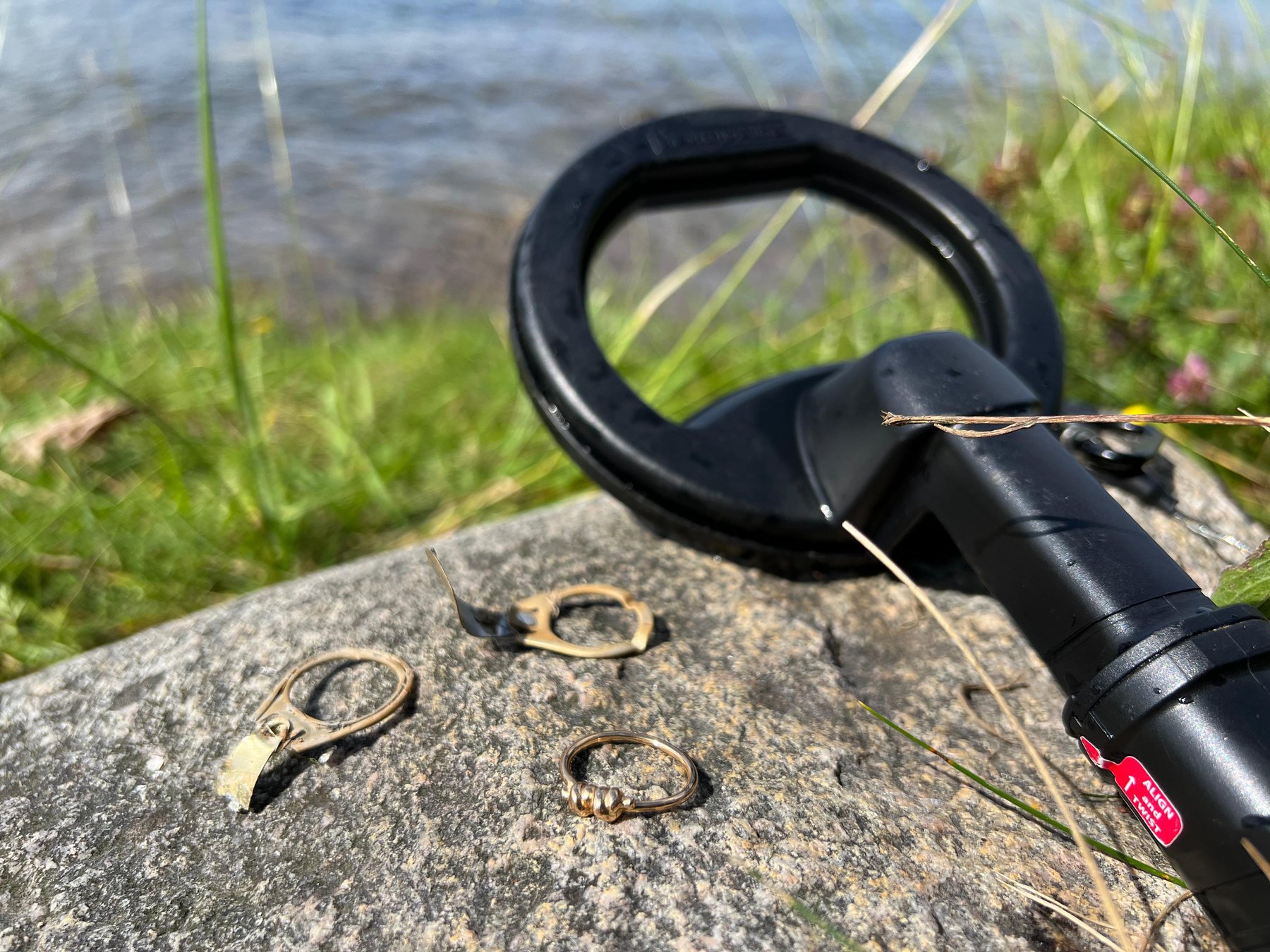 Tre falsklarm och den återfunna guldringen på en klippa vid vattnet, med metalldetektorn i bakgrunden.